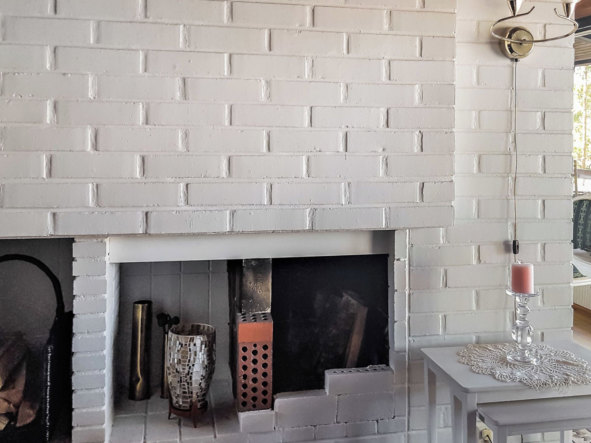 A white brick fireplace with a mantel, a decorative vase, and a candle holder.