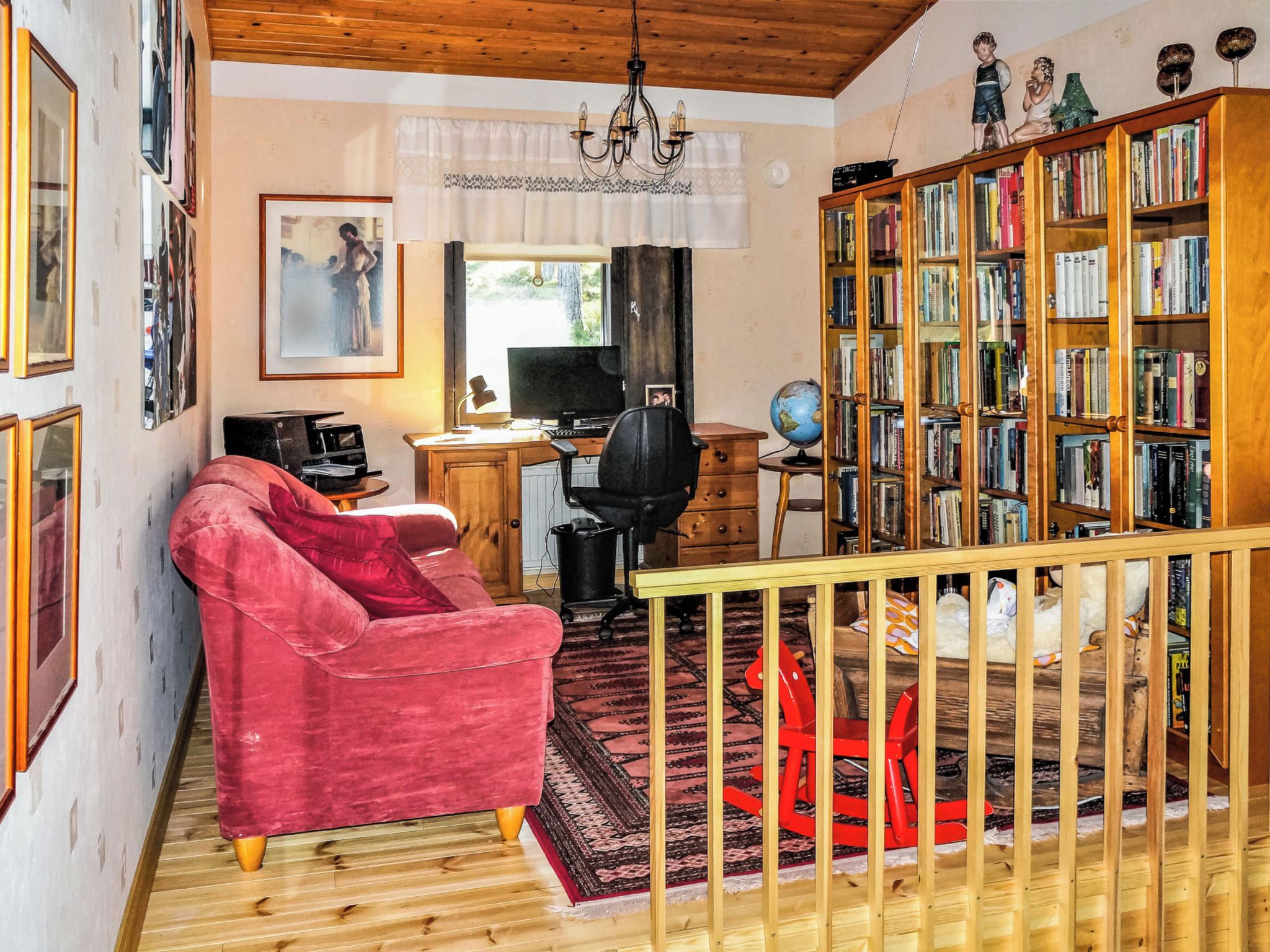 Ein Zimmer mit einem roten Sessel, einem Schreibtisch mit Computer, einem Bücherregal und einem Globus.