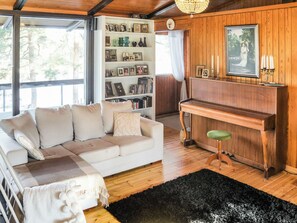 A cozy living room with a white sofa, a wooden piano, and a bookshelf filled with photos and books. - Pippuriranta by Interhome (Sipoo)