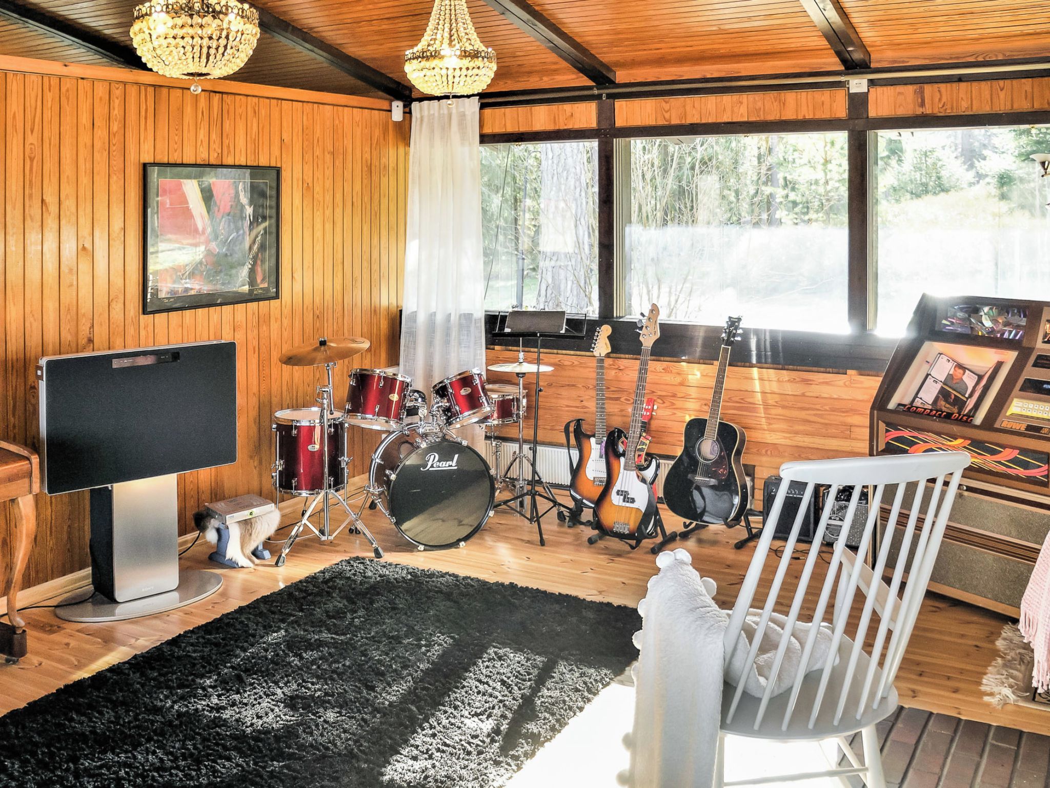 Quarto com decoração em madeira, bateria, guitarras, televisão e berço.