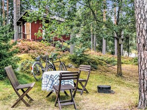 An outdoor seating area with a table and chairs, surrounded by trees and a red building in the background. - Pippuriranta by Interhome (Sipoo)