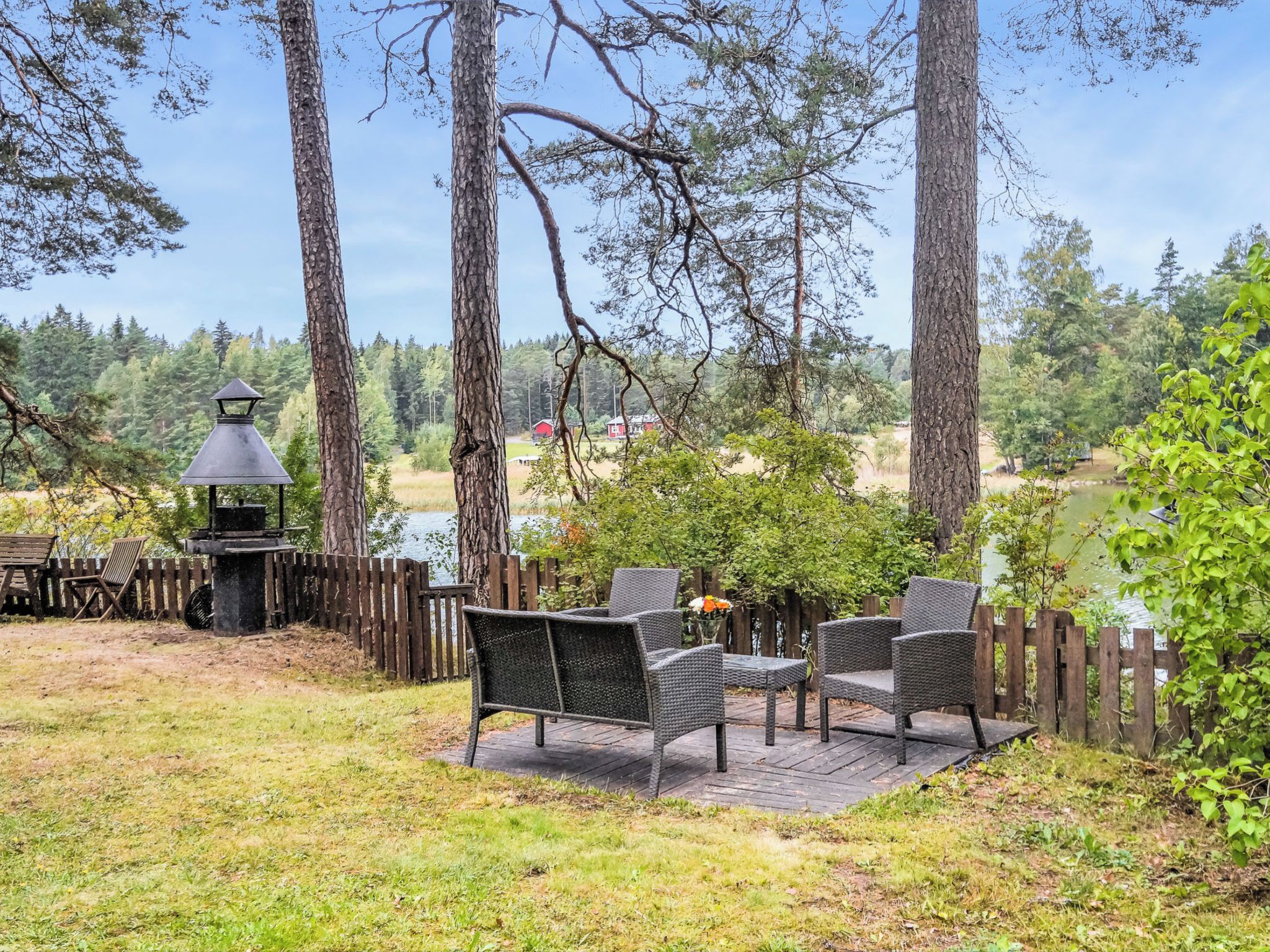 A patio with wicker furniture, a grill, and a view of a lake and forest.