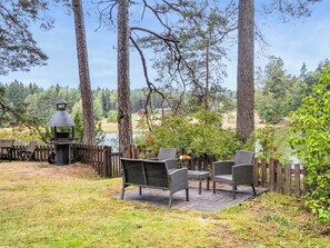 A patio with wicker furniture, a grill, and a view of a lake and forest. - Pippuriranta by Interhome (Sipoo)