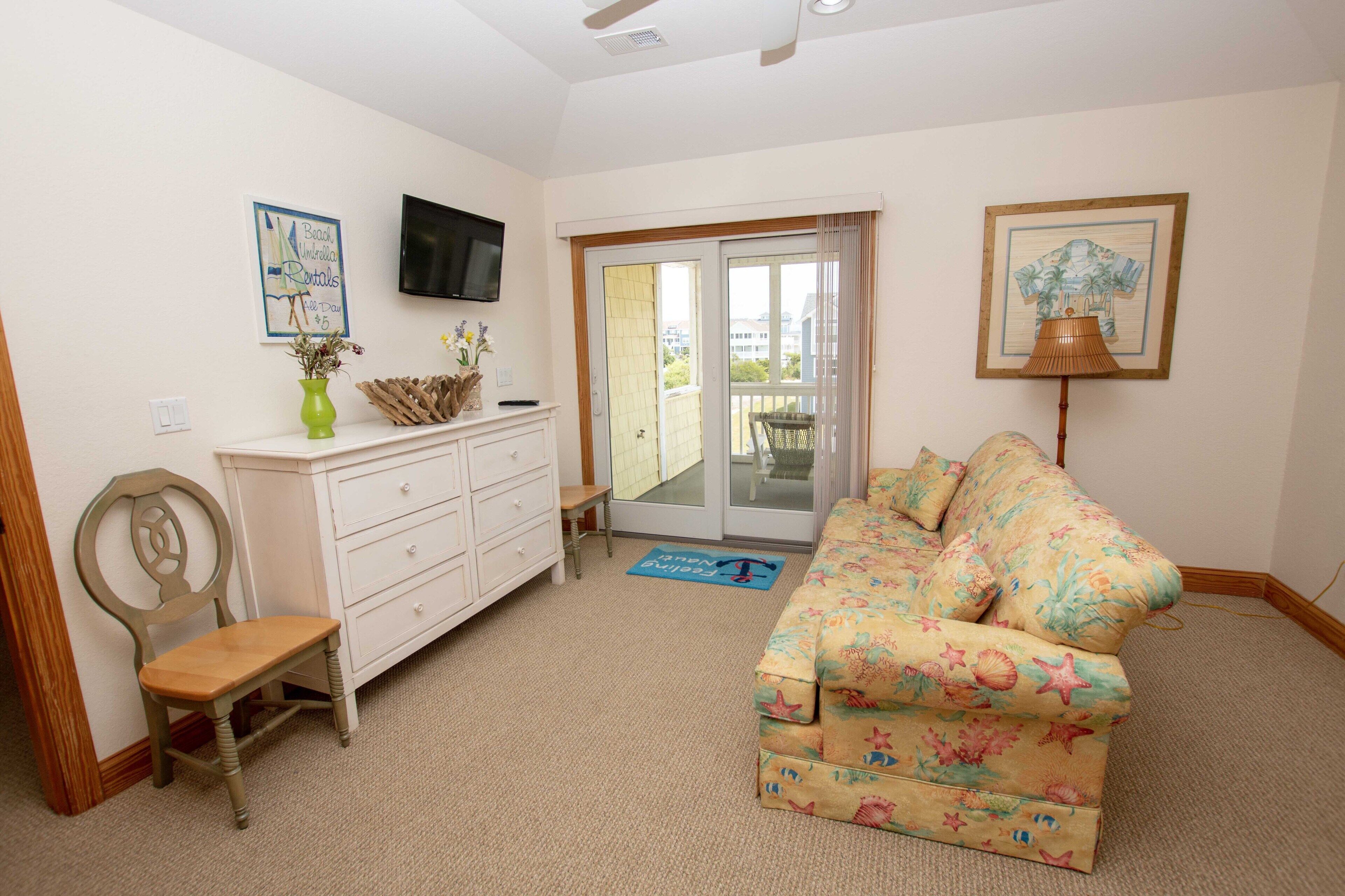 A living room with a sofa, a chair, a TV mounted on the wall, and a door leading to a balcony.
