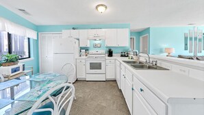 Una cocina moderna con armarios blancos, un lavamanos de acero inoxidable y un comedor con mesa y sillas de vidrio.