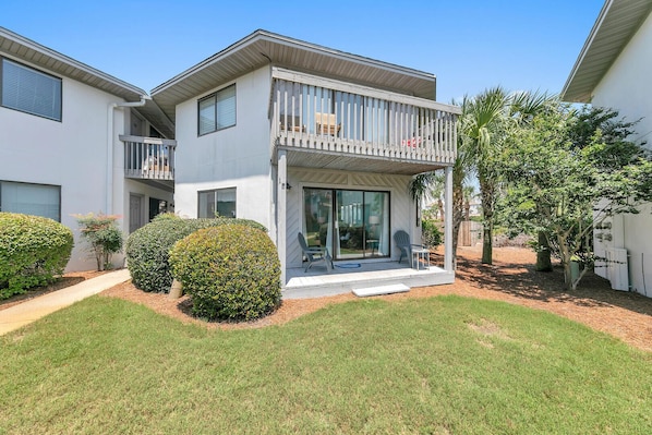 A two-story residential building with a balcony, a covered patio, and a well-maintained lawn.