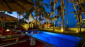 A poolside area with lounge chairs, a small pool, and palm trees at dusk.