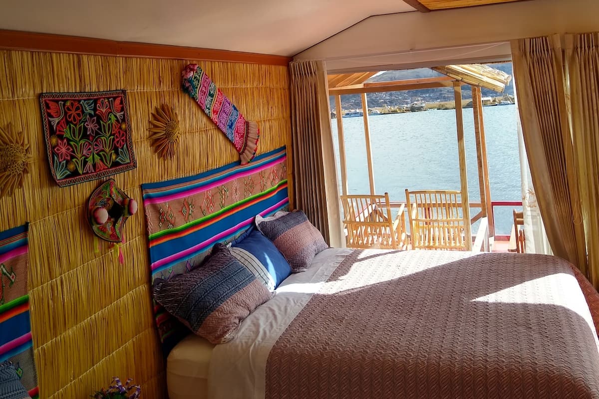 A bedroom with a large bed, a wooden ceiling, and a view of a body of water through a window.