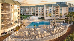 A hotel with multiple balconies, a central pool, and sun loungers arranged around the pool. - Oceanfront at Villamare! Pool and Ocean Views. (Hilton Head Island)