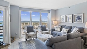 A living room with a view of the beach, striped armchairs, a grey sofa, and a round coffee table. - Oceanfront at Villamare! Pool and Ocean Views. (Hilton Head Island)