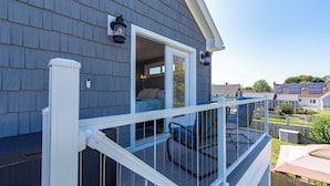 A residential deck with a white railing, a blue chair, and a window overlooking a backyard.