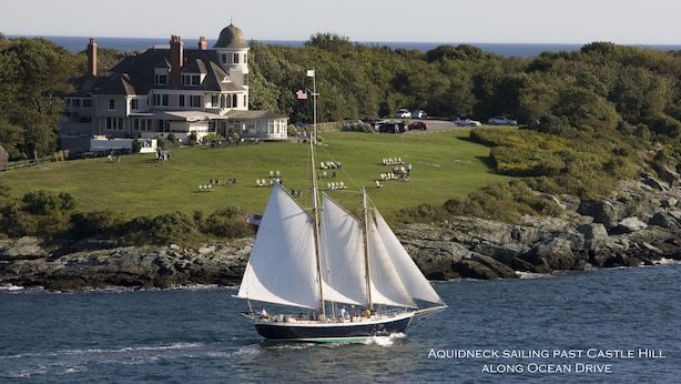 A sailboat on a body of water with a large house in the background.