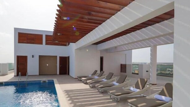 A rooftop pool area with a wooden pergola, lounge chairs, and a clear view of the city skyline. - Belleson Homes The Lennox (Accra)