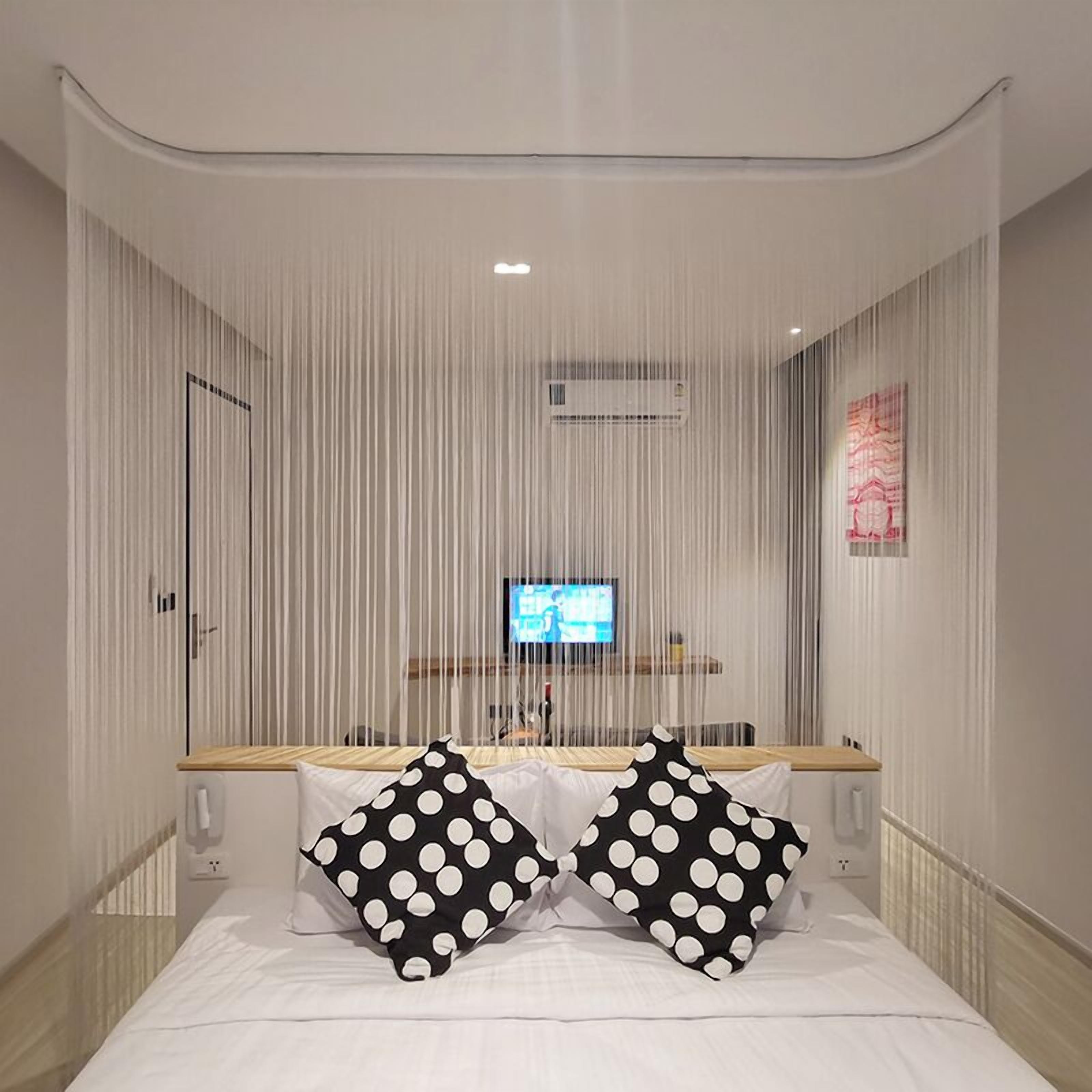 A modern bedroom with a bed, two polka-dotted pillows, a TV on a stand, and a curtain.