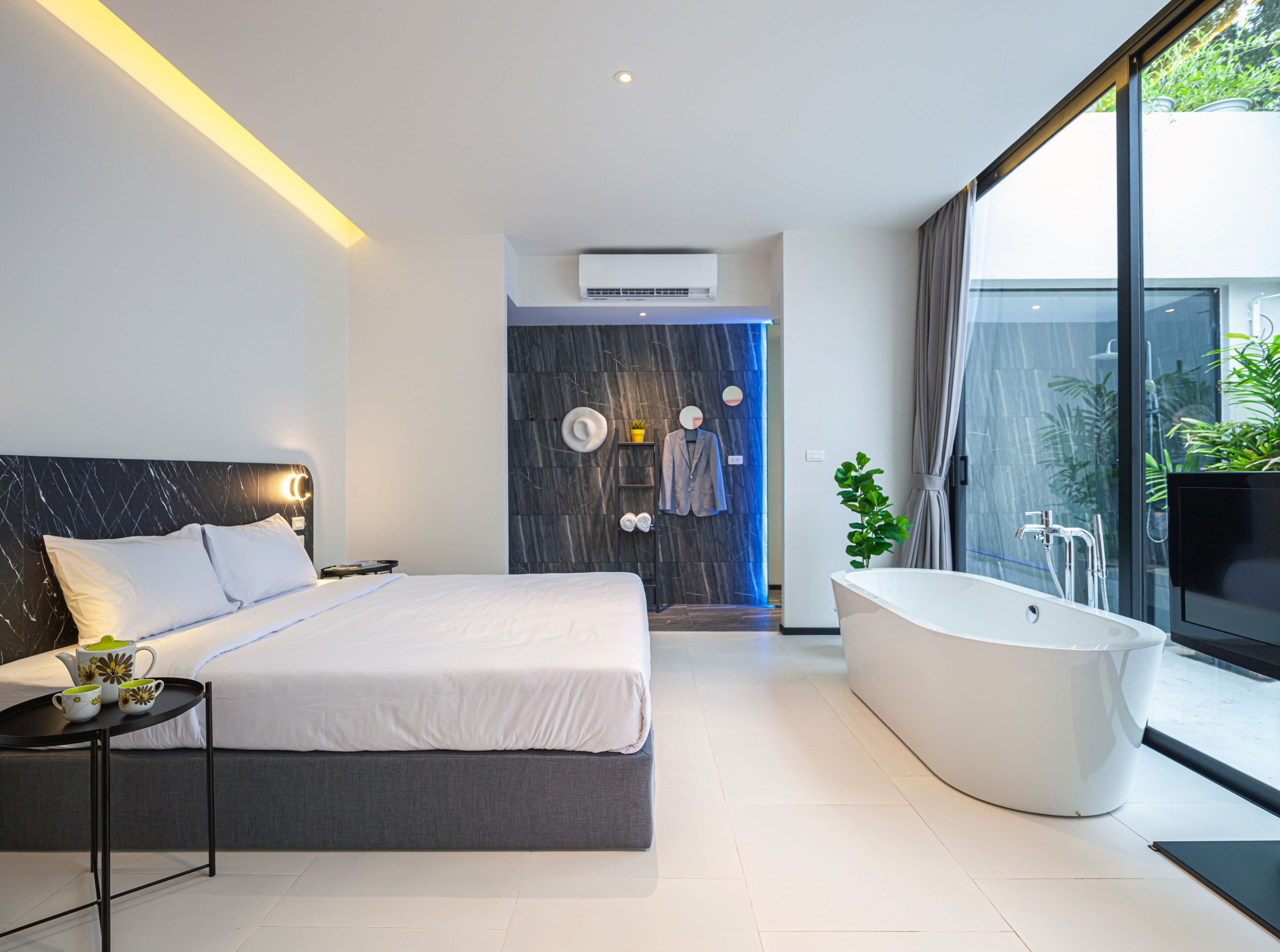 A modern bedroom with a large bed, a built-in bathtub, and a shower area.