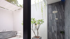 A modern bathroom with a marble shower, a white chair, and a potted plant.