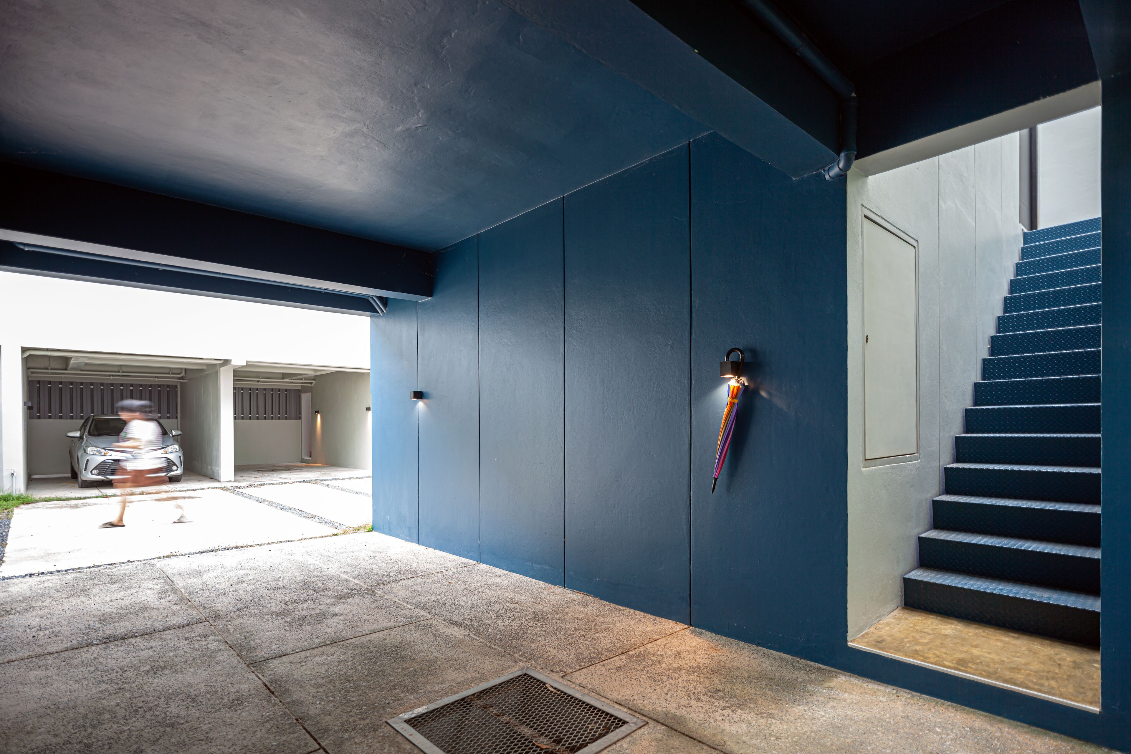 Ein modernes Gebäude mit blauer Fassade, eine Garage mit zwei Autos und eine Treppe, die zu einer oberen Ebene führt.