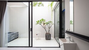 A modern hotel room with a sliding glass door leading to a balcony, a white sink, and a potted plant.