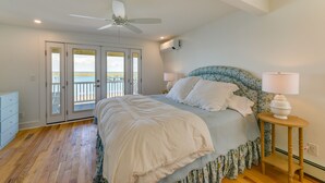 Un dormitorio con cama, ventilador de techo, mesita de noche con lámpara y vista al océano a través de una puerta corrediza.
