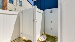 Una cerca de madera blanca con un portón, un muro azul y una pequeña zona de grava con un objeto blanco en el suelo.