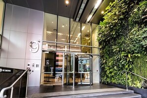 L'ingresso di un edificio moderno con una porta girevole, pareti in vetro e un giardino verticale.