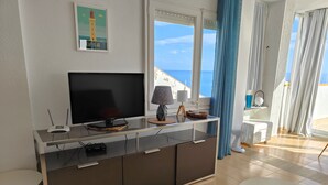 A modern living room with a flat-screen TV, a small table, and a sofa. - VACATION ON THE ROCKS, 1ST LINE OF SEA, PRIVILEGED AREA, SEA VIEW. (Roses)