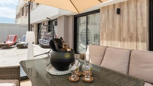 Ein Balkon mit Tisch, Stühlen, einer Rattan-Couch und einem großen Sonnenschirm.