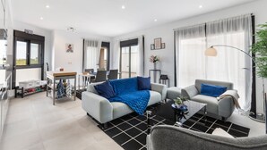 Ein modernes Wohnzimmer mit einer Couch, Sesseln, einem Couchtisch und einem Essbereich mit Tisch und Stühlen.