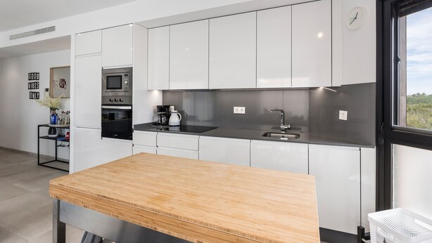 A modern kitchen with white cabinets, a wooden countertop, a built-in microwave, and a window with a view.