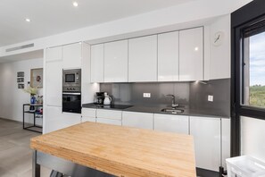 Een moderne keuken met witte kastjes, een houten aanrechtblad, een inbouwmagnetron en een raam met uitzicht.