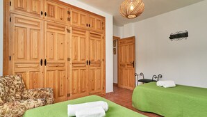 Une pièce avec des armoires en bois, un lit avec une literie verte, un fauteuil à motifs floraux et un luminaire suspendu.