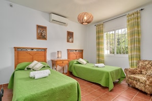 Une chambre d’hôtel avec deux lits, une tête de lit en bois, une petite table, une chaise et une fenêtre avec des rideaux.