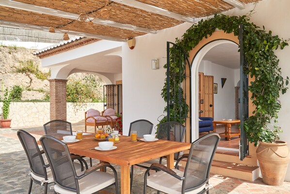 Un espace de restauration en plein air avec une table et des chaises en bois, entouré de verdure et d’un mur en pierre.