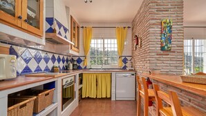 Une cuisine avec un mur en briques, une fenêtre ornée de rideaux jaunes et un pare-feu en carreaux.