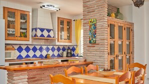 Une cuisine avec un pilier en briques, des armoires en bois et un coin repas comprenant des chaises et une table.