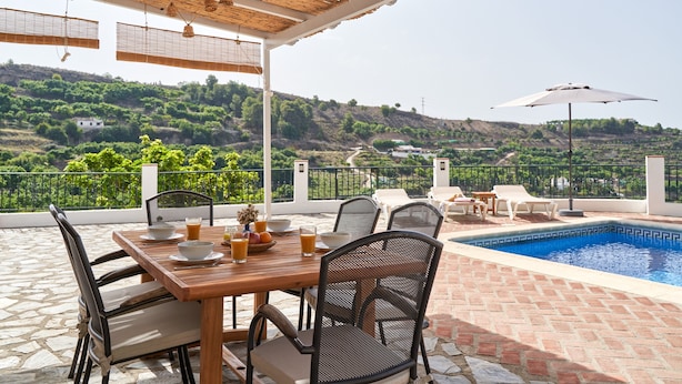 Un espace extérieur abrité comprenant une piscine, une table à manger, des chaises et une vue sur un paysage vallonné.