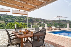 Un espace extérieur abrité comprenant une piscine, une table à manger, des chaises et une vue sur un paysage vallonné.