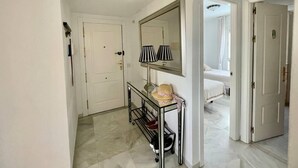 A hallway with a white door, a mirror, a lamp, and a small table with a hat. - Stunning 2Bed Apartment in Marbella - Pto Banus (Marbella)