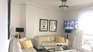 A modern living room with a beige sofa, a glass coffee table, and a flat-screen TV mounted on the wall. - Stunning 2Bed Apartment in Marbella - Pto Banus (Marbella)