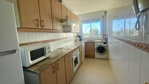 A compact kitchen with wooden cabinets, a microwave, a washing machine, and a window with butterfly decals. - Stunning 2Bed Apartment in Marbella - Pto Banus (Marbella)