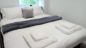 Ein ordentlich gemachtes Bett mit weißen Laken, einer grauen Decke und gefalteten weißen Handtüchern.