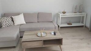 Un salon moderne avec un canapé gris, une table basse en bois avec un plateau, et une table d’appoint blanche agrémentée d’objets décoratifs.