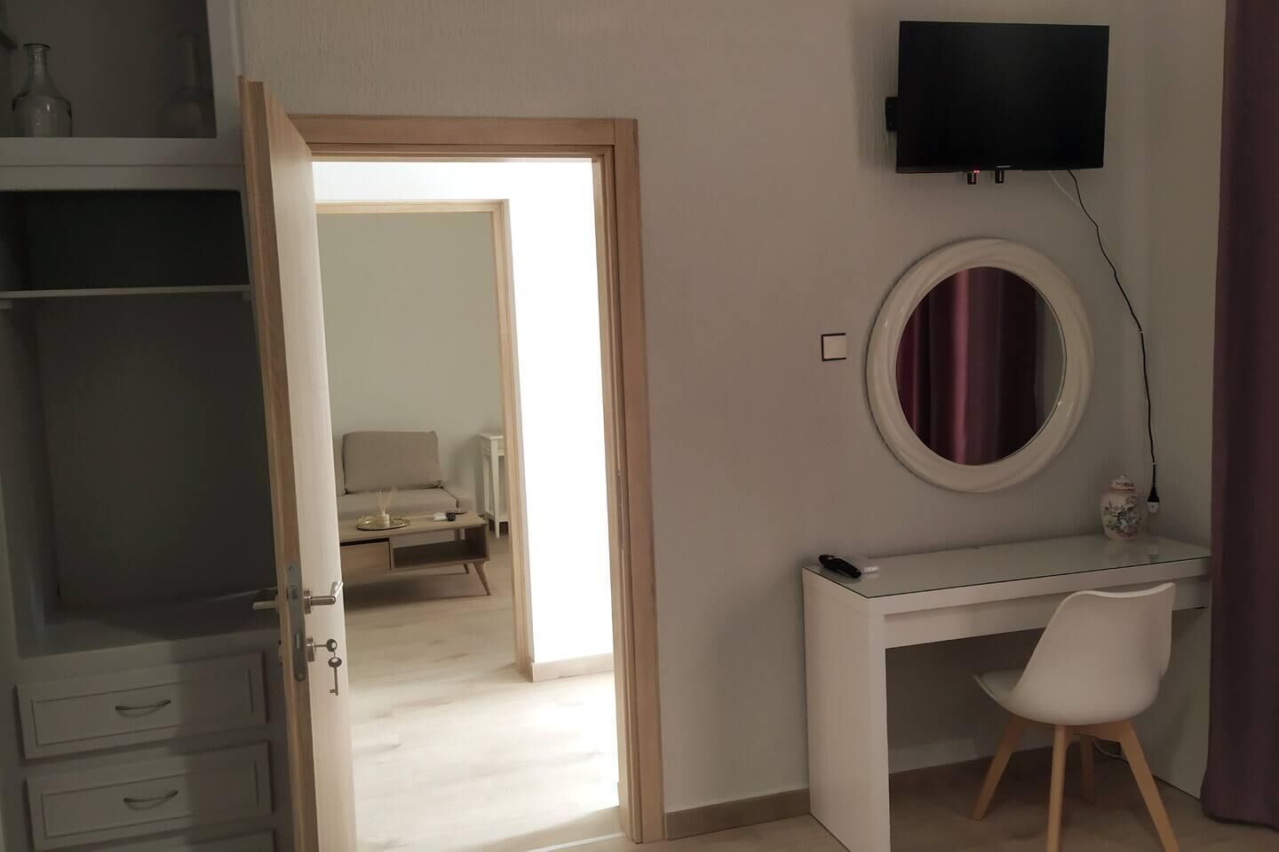 Ein Zimmer mit Schreibtisch, Stuhl, Wandfernseher und einer Tür zu einem anderen Raum.