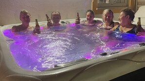 Un groupe de personnes dans un jacuzzi éclairé de lumières violettes, avec un luminaire fixé au mur et une fenêtre donnant sur l’extérieur.
