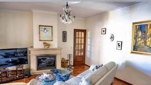 Un salon avec une cheminée, un canapé, un téléviseur et un lustre.