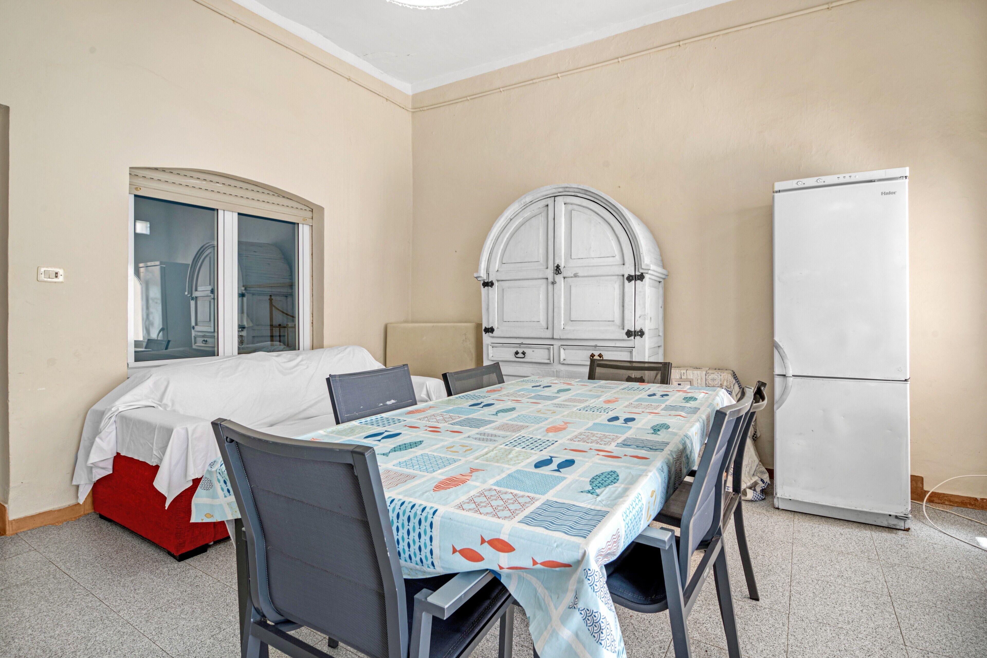 Una habitación con cama, una mesa con sillas, un refrigerador y un ventanal con cortinas.