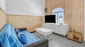 A room with a bed, a white desk, a TV, and a window with a view.