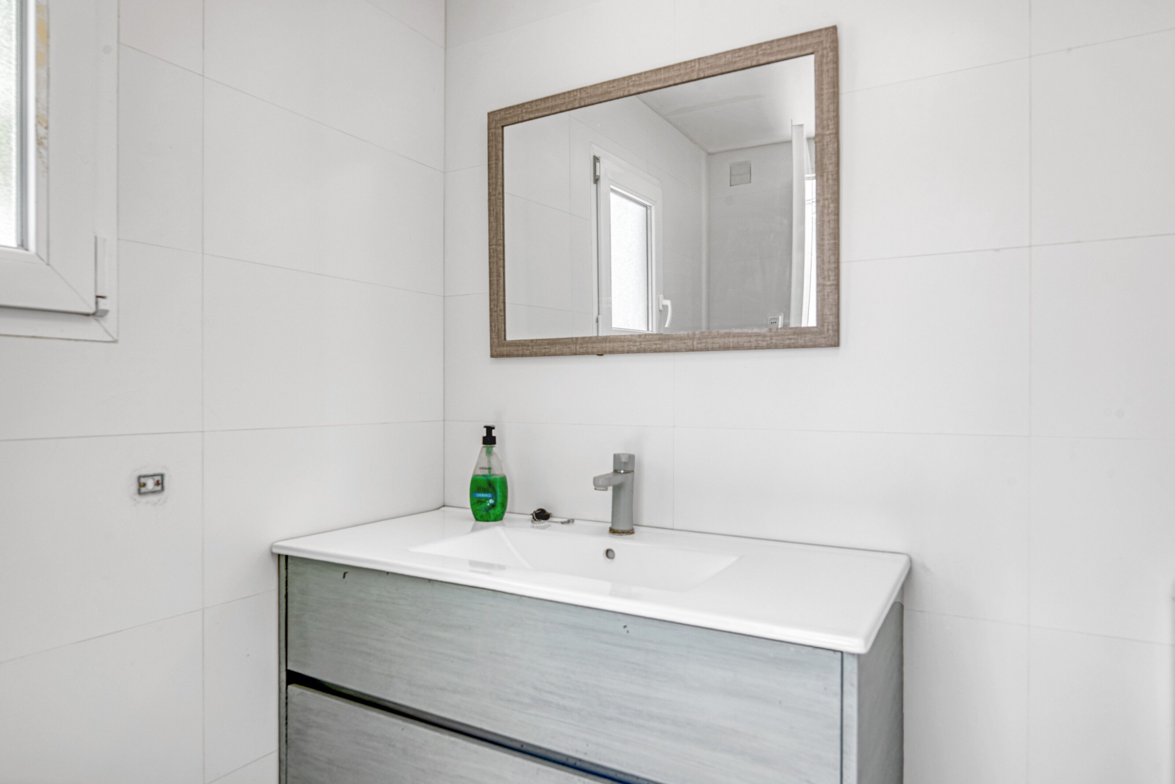 Une salle de bain avec un lavabo blanc, un miroir et un flacon de savon vert.