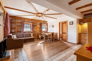 Una stanza accogliente con ventilatore a soffitto in legno, un tavolo da pranzo con sedie, un divano e un angolo cottura con pensili in legno.