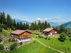 Un village de montagne aux maisons traditionnelles en bois, avec un puits en pierre et une vue dégagée sur la forêt et les montagnes environnantes.